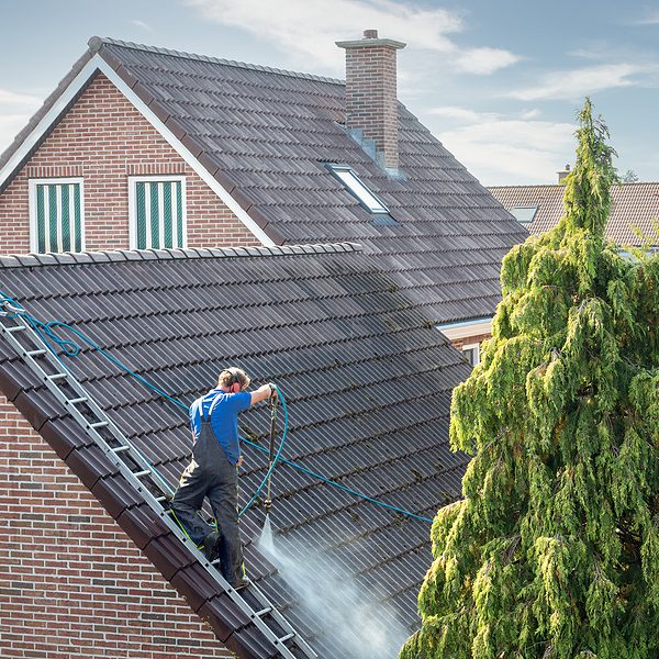 Cleaner with pressure washer at roof of house cleaning the roof tiles, removing moss and weed